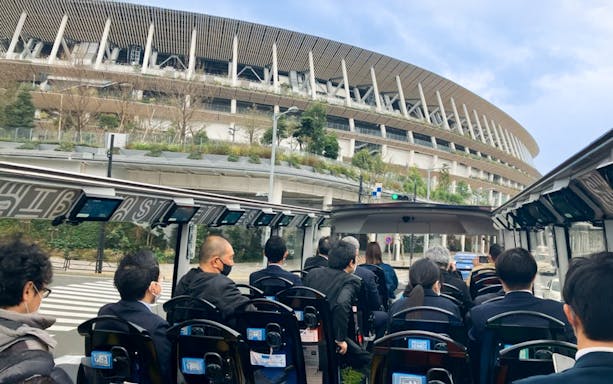 Open-top bus tour passing Tokyo's National Stadium.