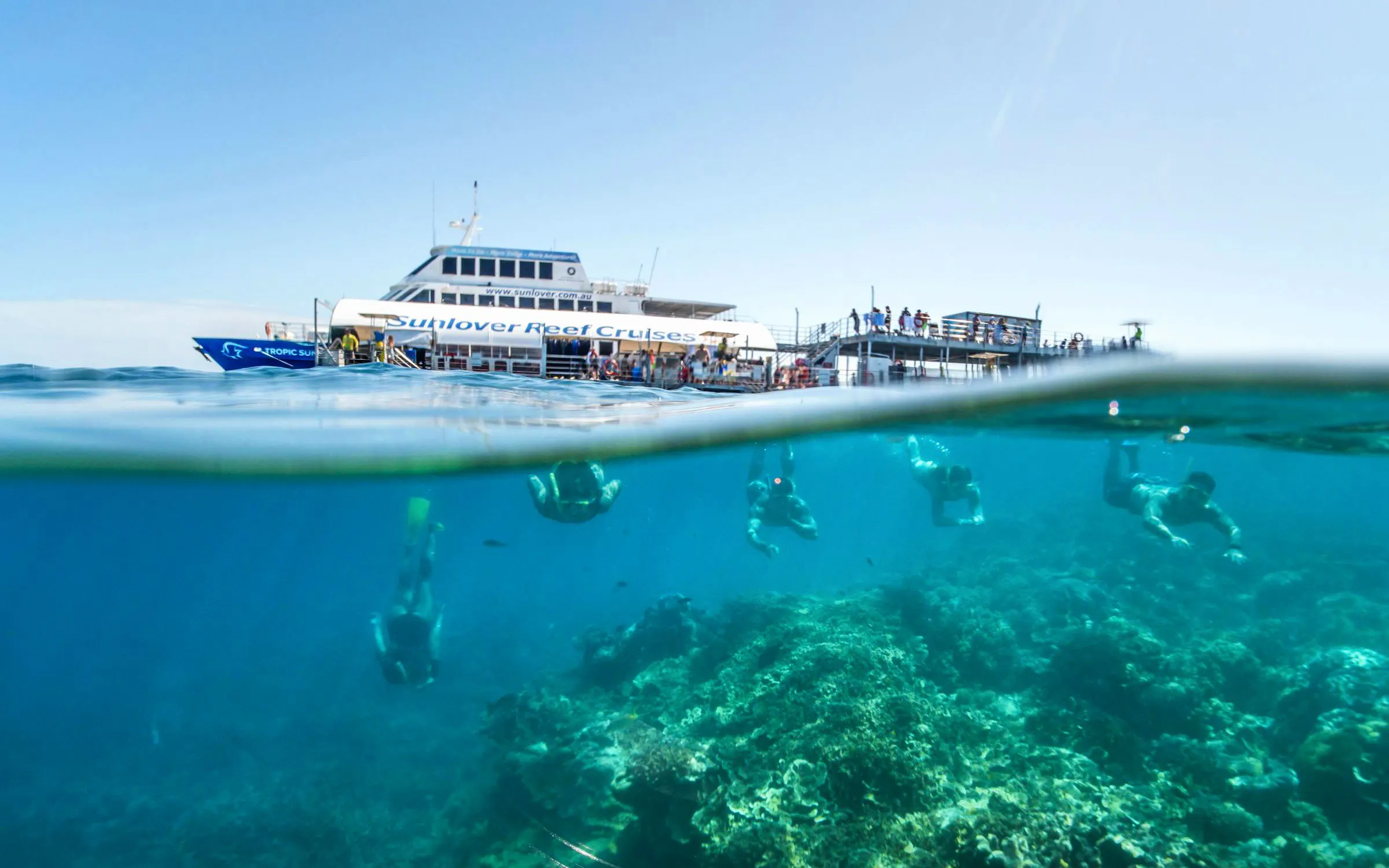 Snorkelers exploring coral beneath Sunlover Reef Cruises boat at Great Barrier Reef.