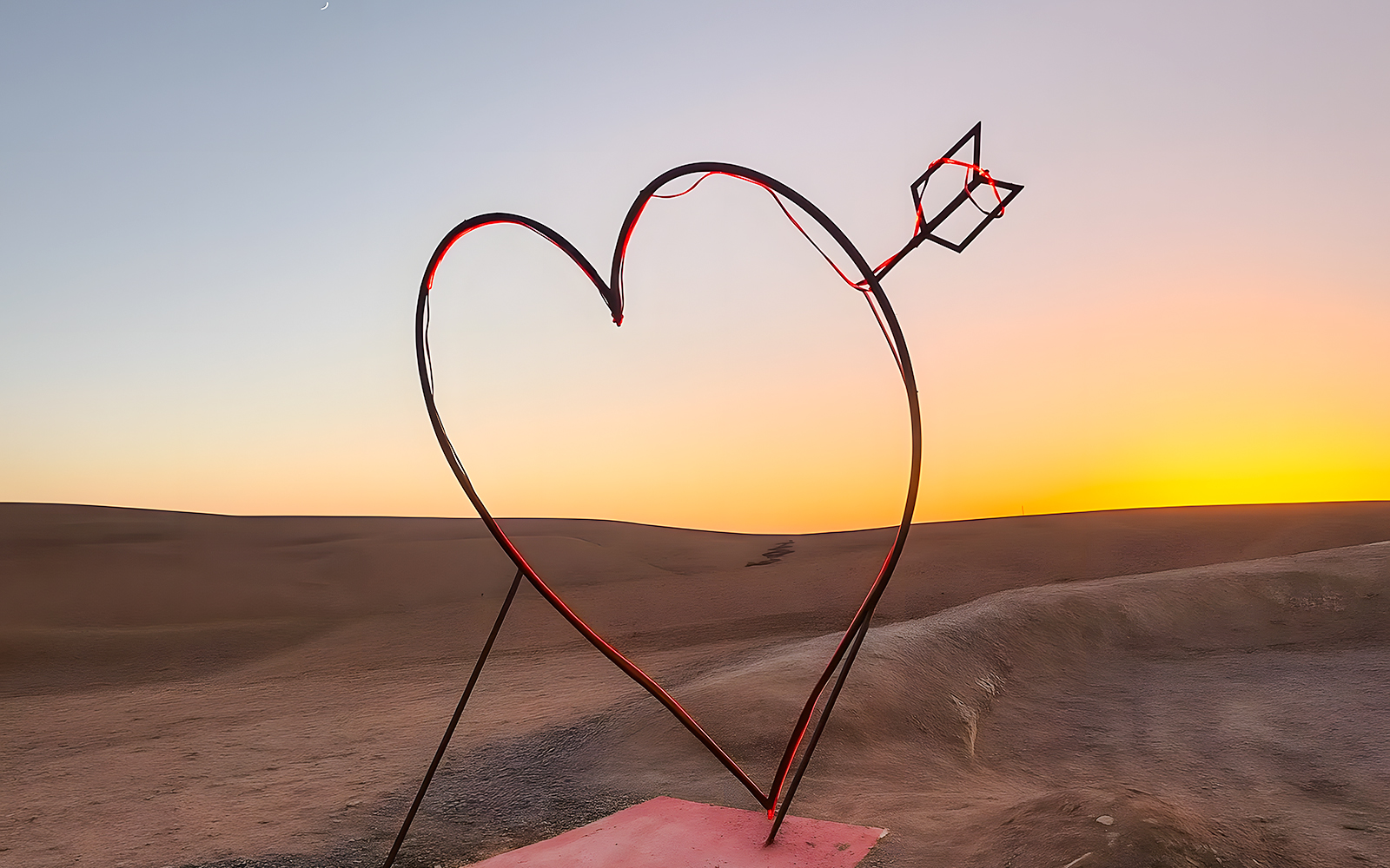 Heart-shaped sculpture with arrow in Agafay Desert, Marrakech at sunset.
