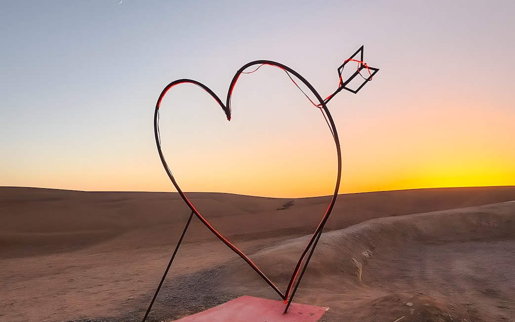Heart-shaped sculpture with arrow in Agafay Desert, Marrakech at sunset.