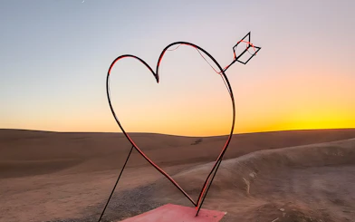 Heart-shaped sculpture with arrow in Agafay Desert, Marrakech at sunset.