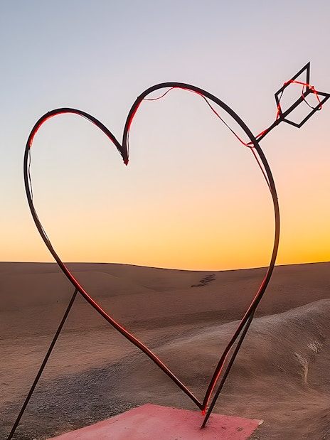 Heart-shaped sculpture with arrow in Agafay Desert, Marrakech at sunset.