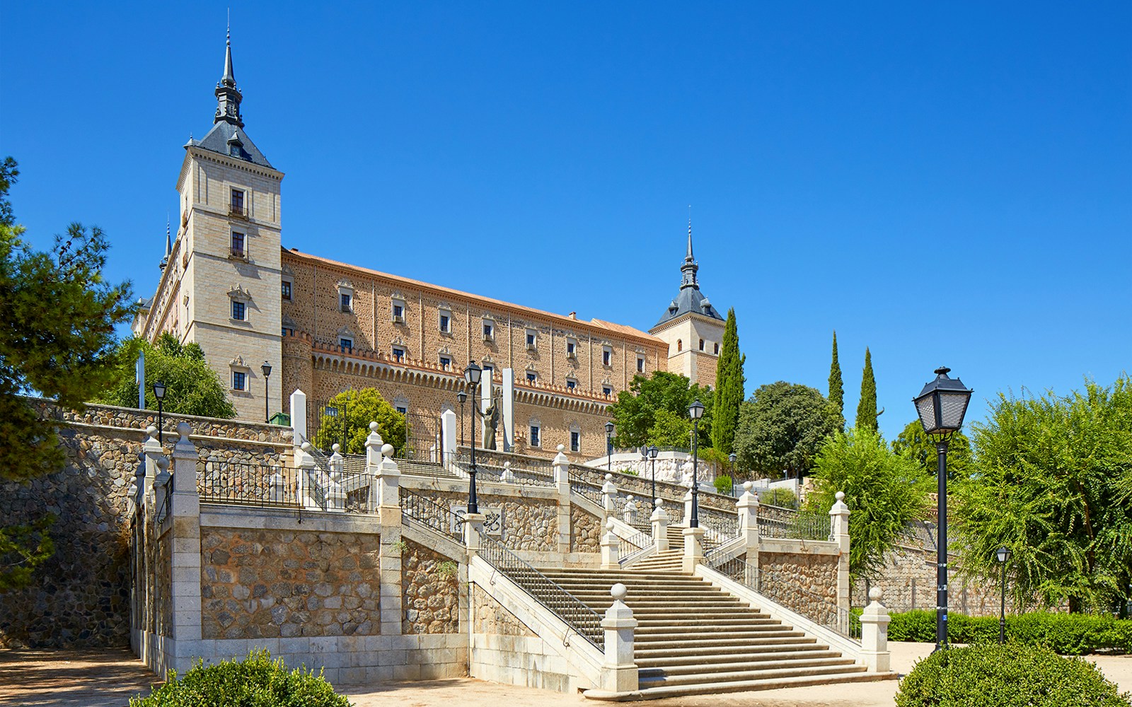 Alcazar of Toledo with stone steps and towers under a clear blue sky, Spain.