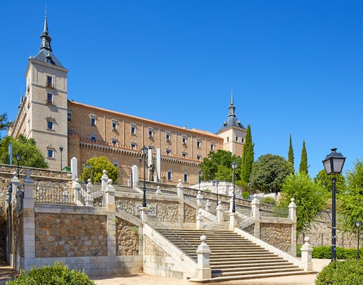 Alcazar of Toledo with stone steps and towers under a clear blue sky, Spain.