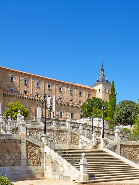 Alcazar of Toledo with stone steps and towers under a clear blue sky, Spain.