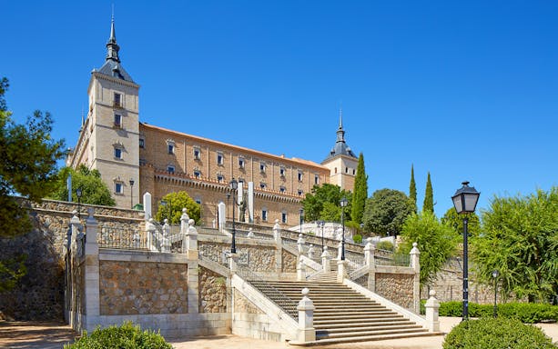 Alcazar of Toledo with stone steps and towers under a clear blue sky, Spain.