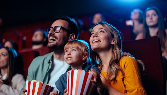 Family enjoying a movie at a global cinema, holding popcorn.