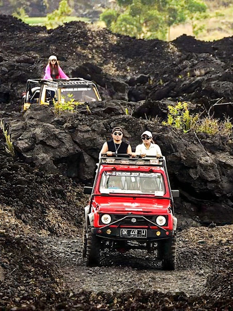 People driving jeeps on black lava trails at Mount Batur, Bali.
