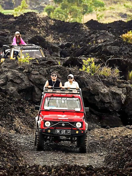 People driving jeeps on black lava trails at Mount Batur, Bali.