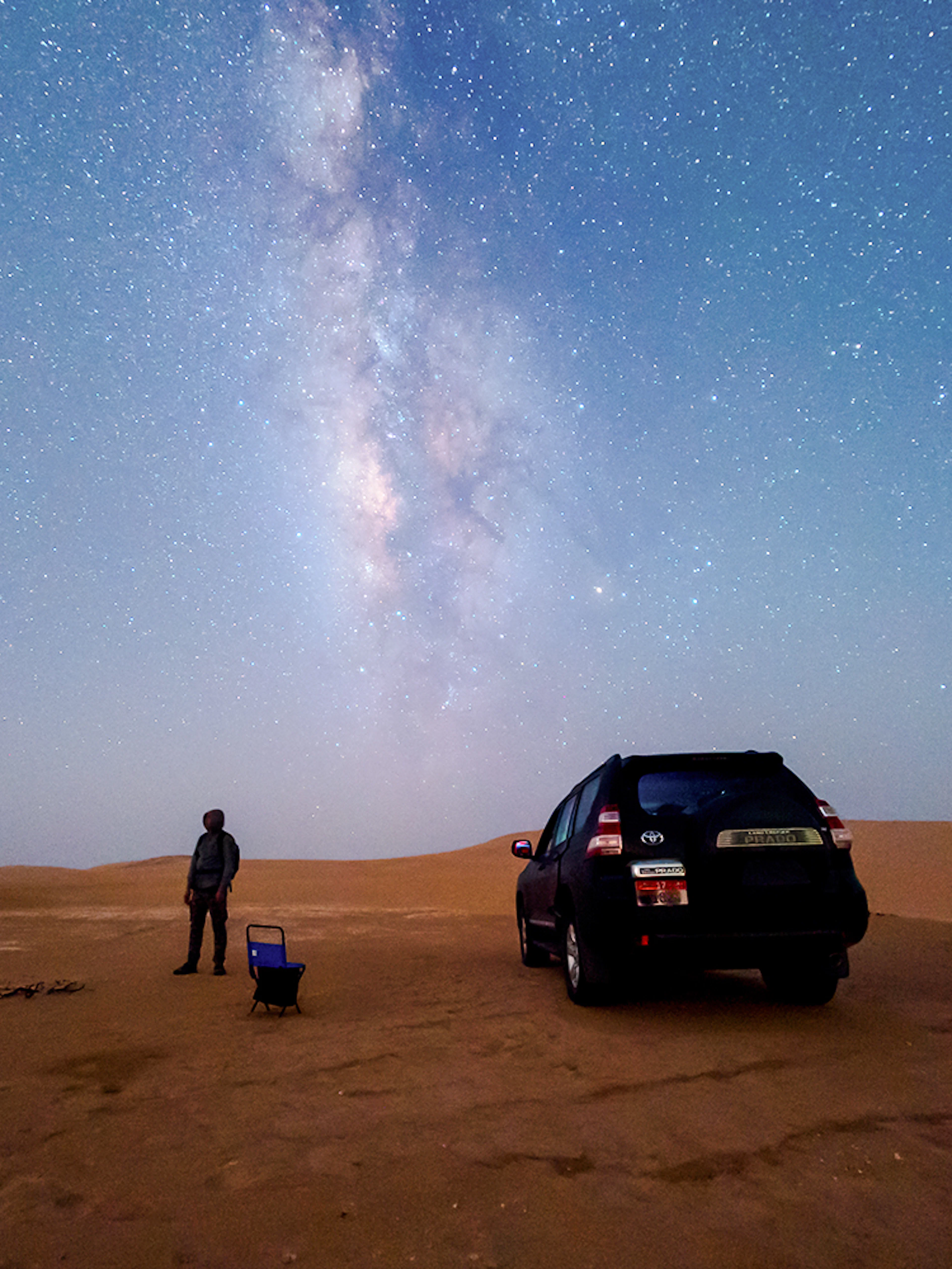 Milky Way over desert sand dune with person and parked car.