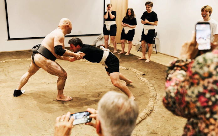 Sumo wrestler and participant engage in a match during Osaka sumo experience.