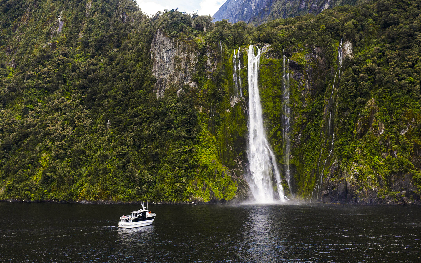 Sinbad cruise ship near waterfall in Milford Sound, New Zealand.