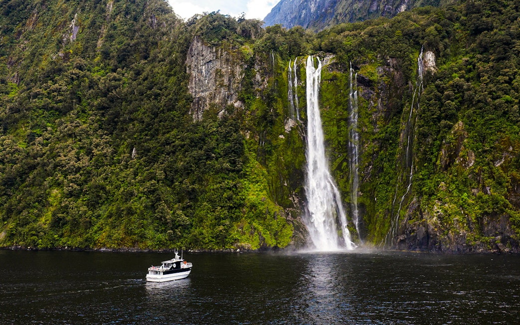 Sinbad cruise ship near waterfall in Milford Sound, New Zealand.