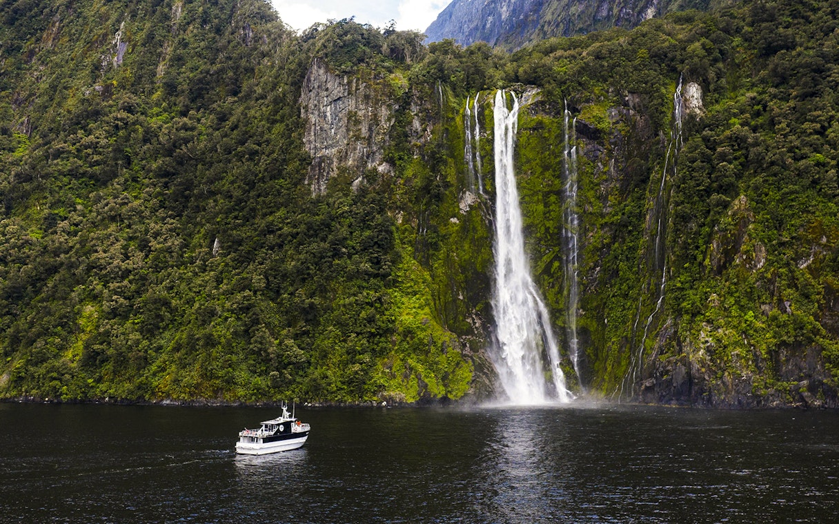 Sinbad cruise ship near waterfall in Milford Sound, New Zealand.
