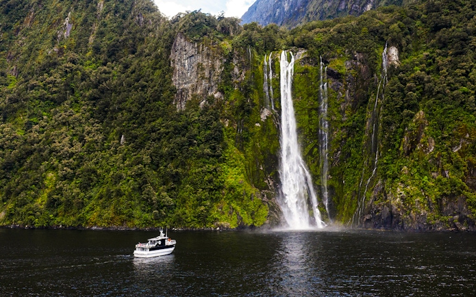 Sinbad cruise ship near waterfall in Milford Sound, New Zealand.