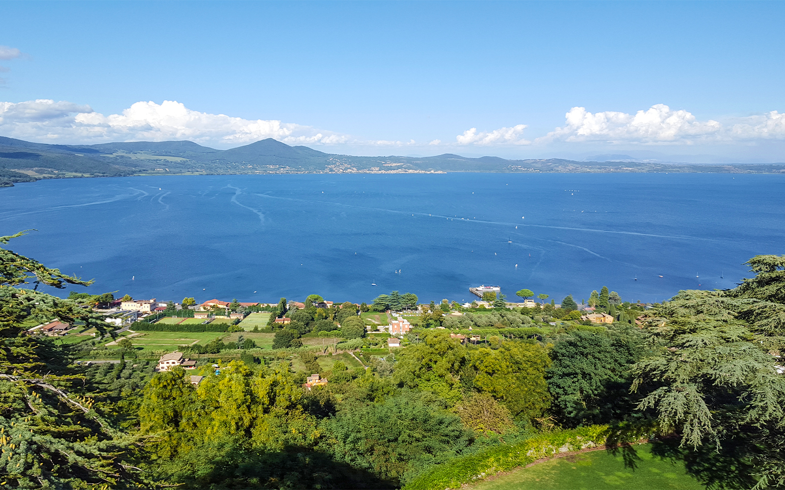 Aerial view of Lake Bracciano with surrounding greenery and distant mountains.