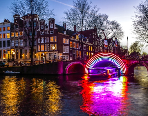 Canal boat under illuminated arch at Amsterdam Light Festival.