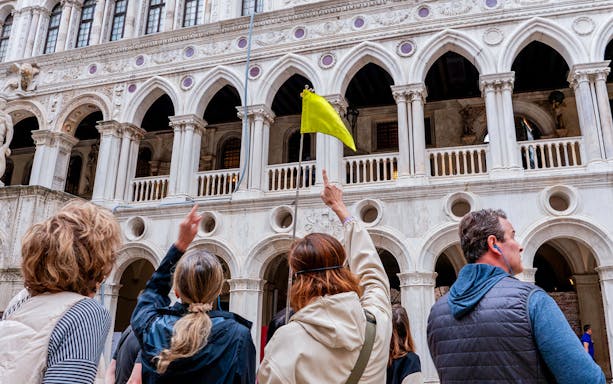 Tour group at Doge's Palace, Venice, with guide holding yellow flag.