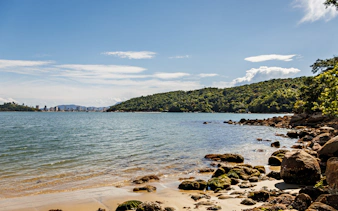 Araça Beach in Brazil with rocky shoreline and distant city skyline.