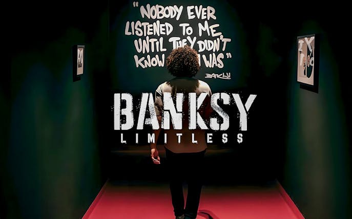 Visitor at Banksy Limitless exhibition viewing artwork with quote on wall.