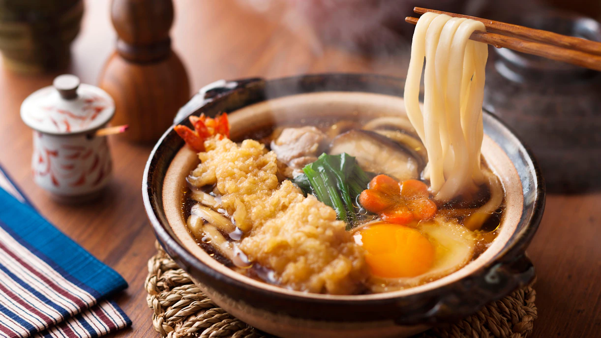 Nabeyaki udon with tempura shrimp, egg, and vegetables in a steaming pot.