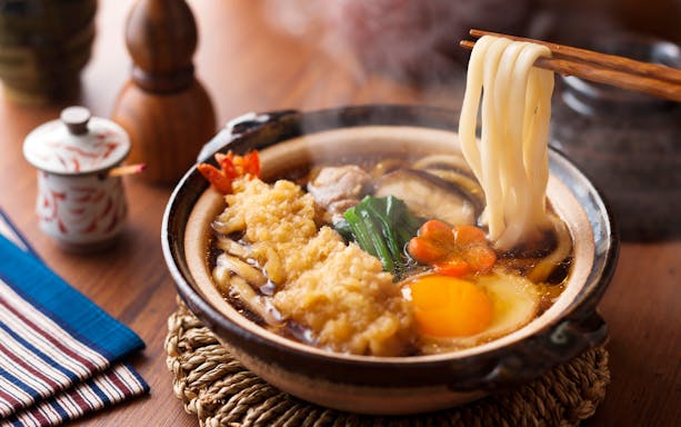 Nabeyaki udon with tempura shrimp, egg, and vegetables in a steaming pot.