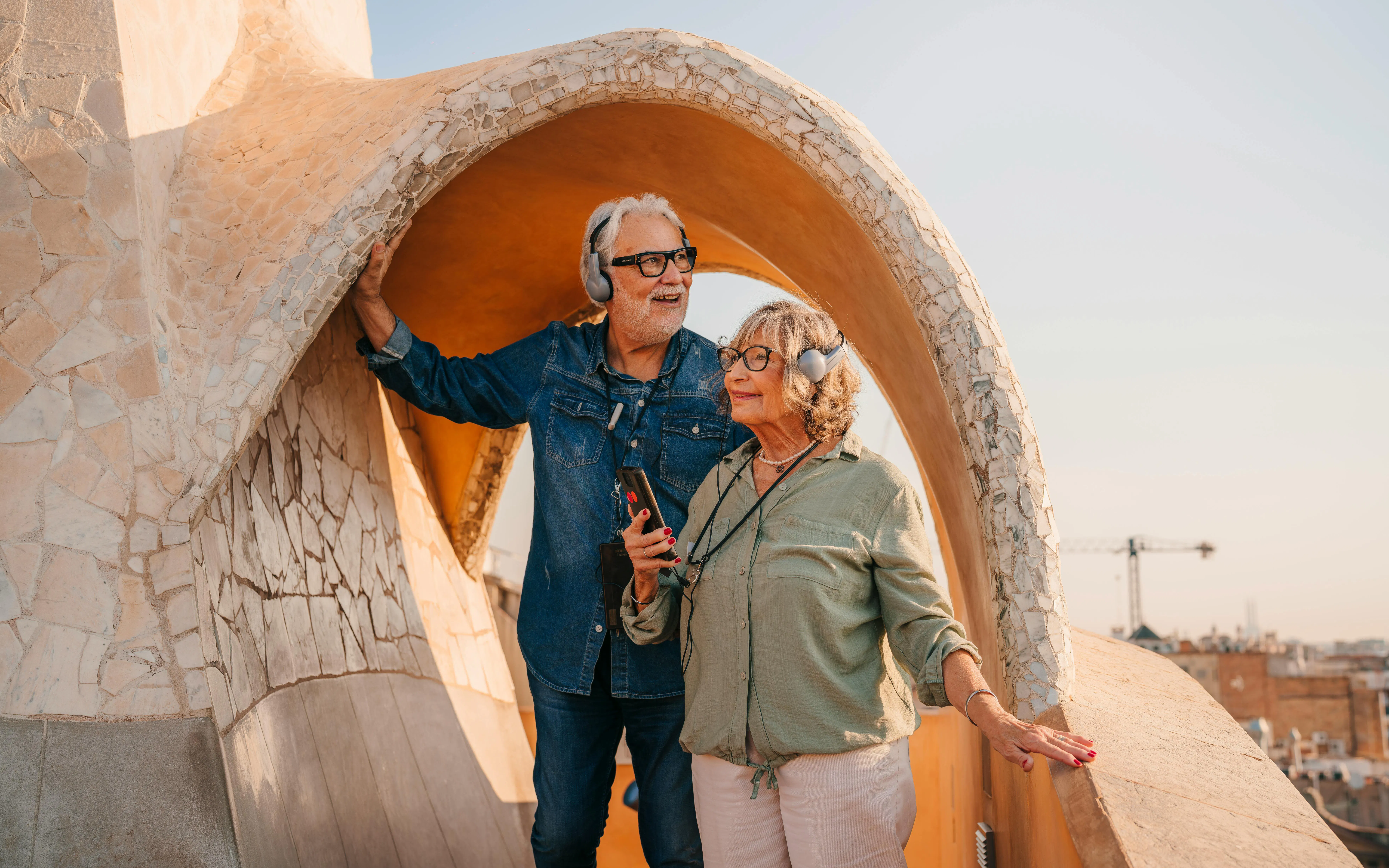 Couple enjoying audio tour on La Pedrera rooftop at sunset, Barcelona.