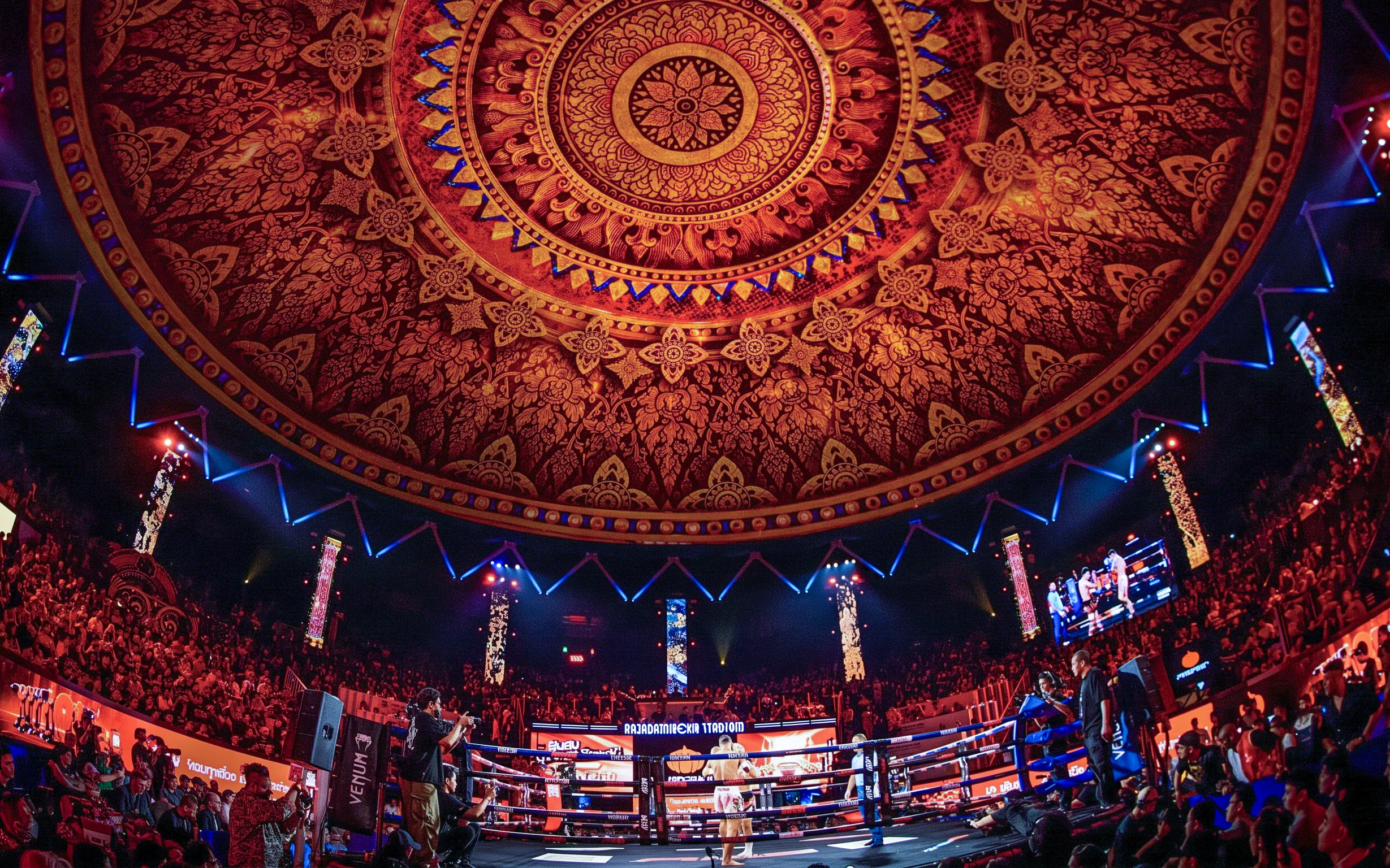 Boxing match at Rajadamnern Stadium under ornate ceiling.