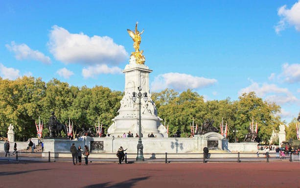 Victoria Memorial near Buckingham Palace, London, with tourists and trees in the background.