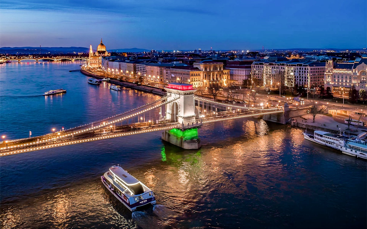 Cruise boat on Danube River near illuminated Chain Bridge in Budapest at night.