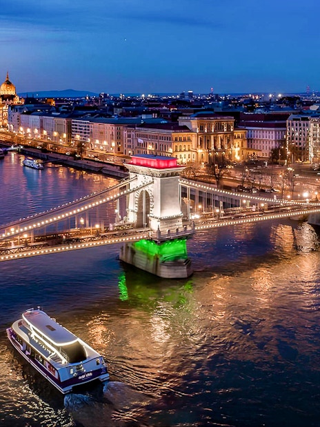 Cruise boat on Danube River near illuminated Chain Bridge in Budapest at night.