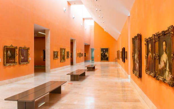 Interior of Thyssen-Bornemisza Museum in Madrid with classic paintings on orange walls.