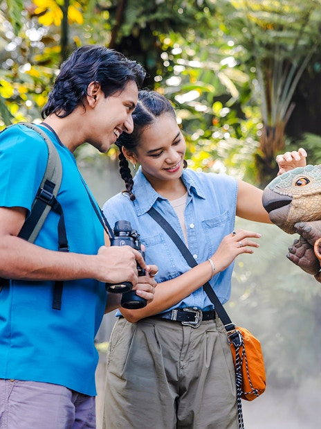 Visitors interacting with a dinosaur puppet at Jurassic World, Cloud Forest, Gardens by the Bay, Singapore.