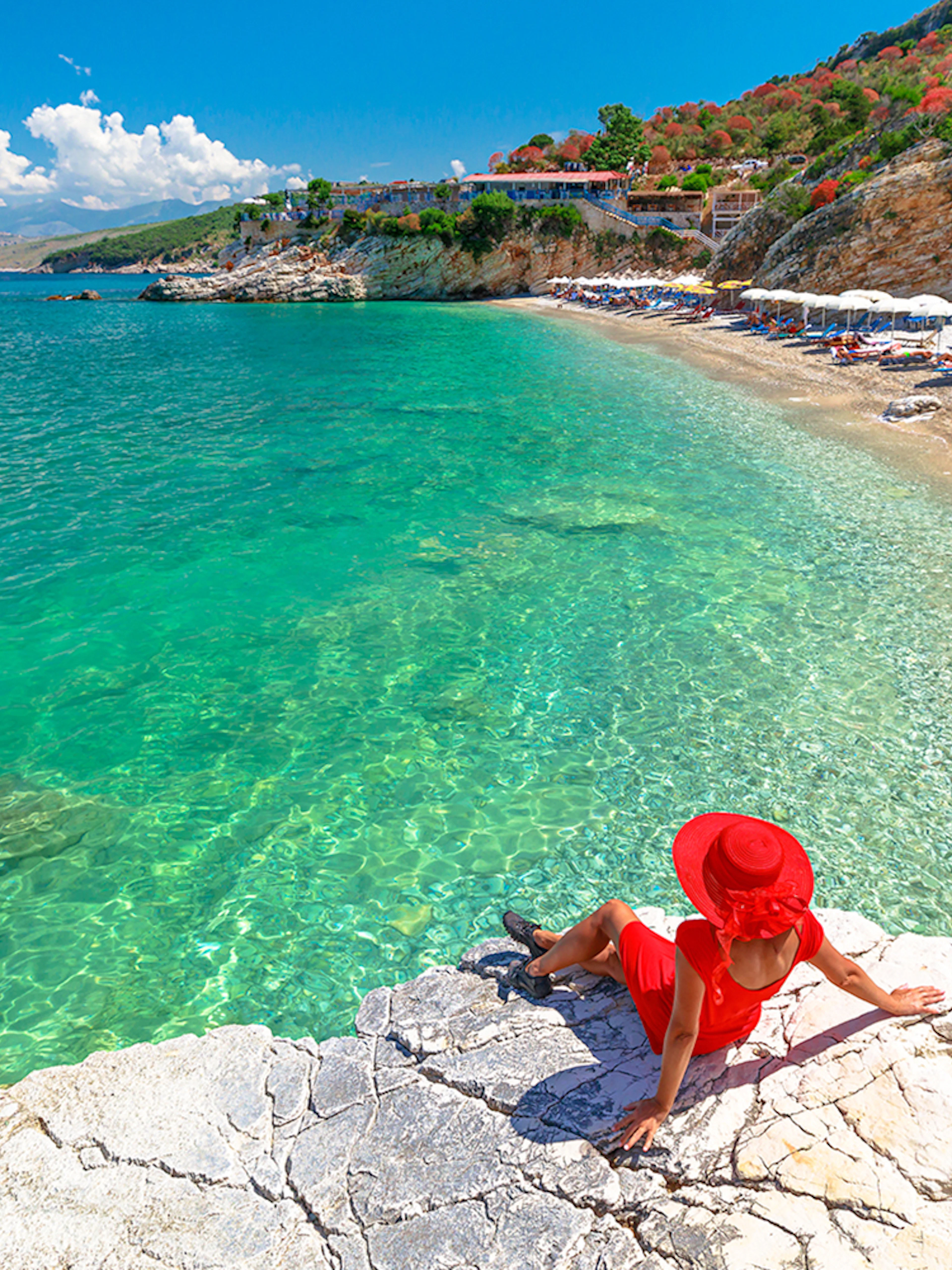 Sunbathing guest on rocky shore near Saranda, Albania with clear turquoise water.