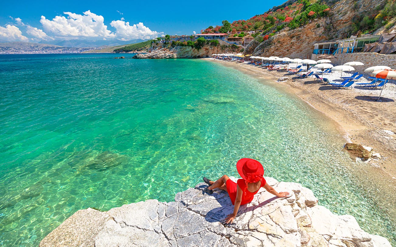 Sunbathing guest on rocky shore near Saranda, Albania with clear turquoise water.