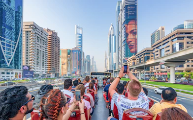 Tourists on a Dubai hop-on hop-off bus tour capturing city skyscrapers along Sheikh Zayed Road.