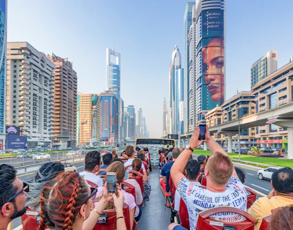 Tourists on a Dubai hop-on hop-off bus tour capturing city skyscrapers along Sheikh Zayed Road.