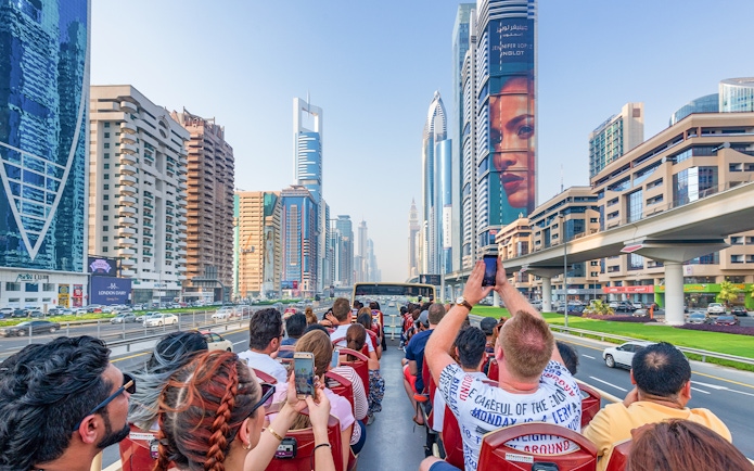 Tourists on a Dubai hop-on hop-off bus tour capturing city skyscrapers along Sheikh Zayed Road.