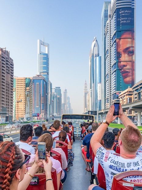 Tourists on a Dubai hop-on hop-off bus tour capturing city skyscrapers along Sheikh Zayed Road.