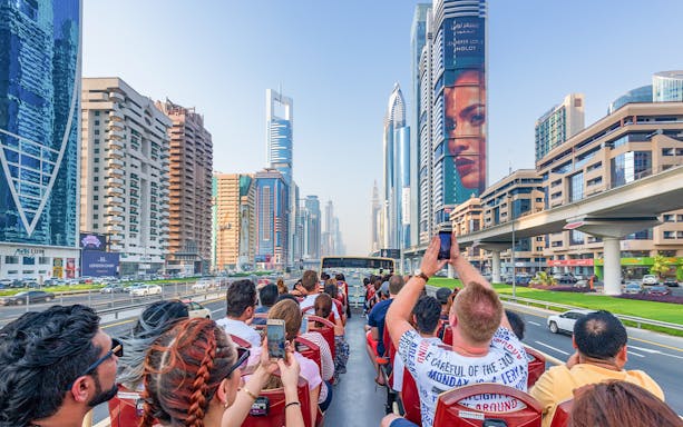 Tourists on a Dubai hop-on hop-off bus tour capturing city skyscrapers along Sheikh Zayed Road.