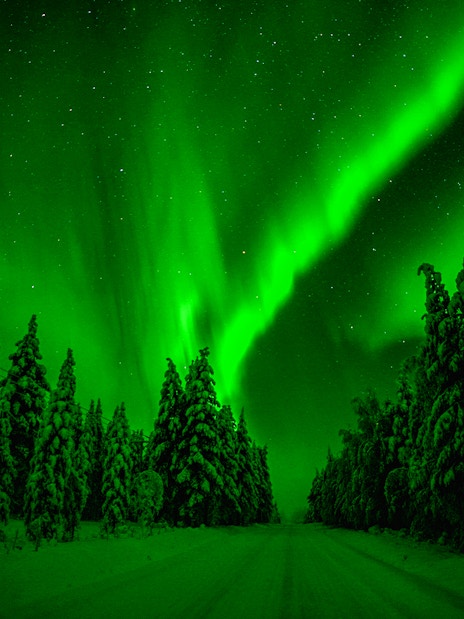Snowmobiles on snowy path under Northern Lights in Rovaniemi, Finland.