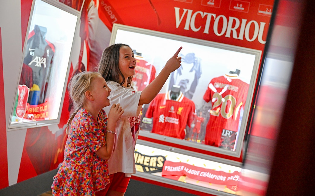 Children exploring Liverpool FC Museum at Anfield, viewing championship jerseys.