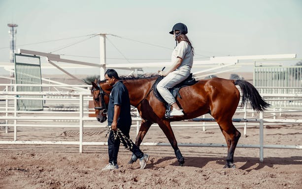 Person riding a horse led by a guide at Mleiha Arena.