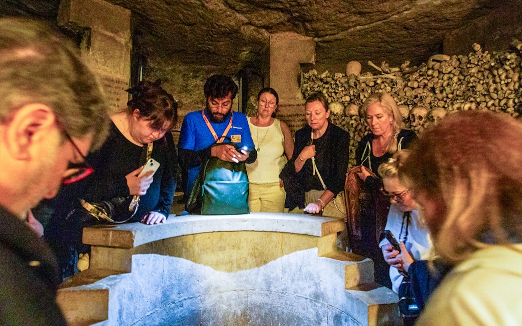Tourists exploring the Paris Catacombs, viewing skulls and bones in dimly lit tunnels.