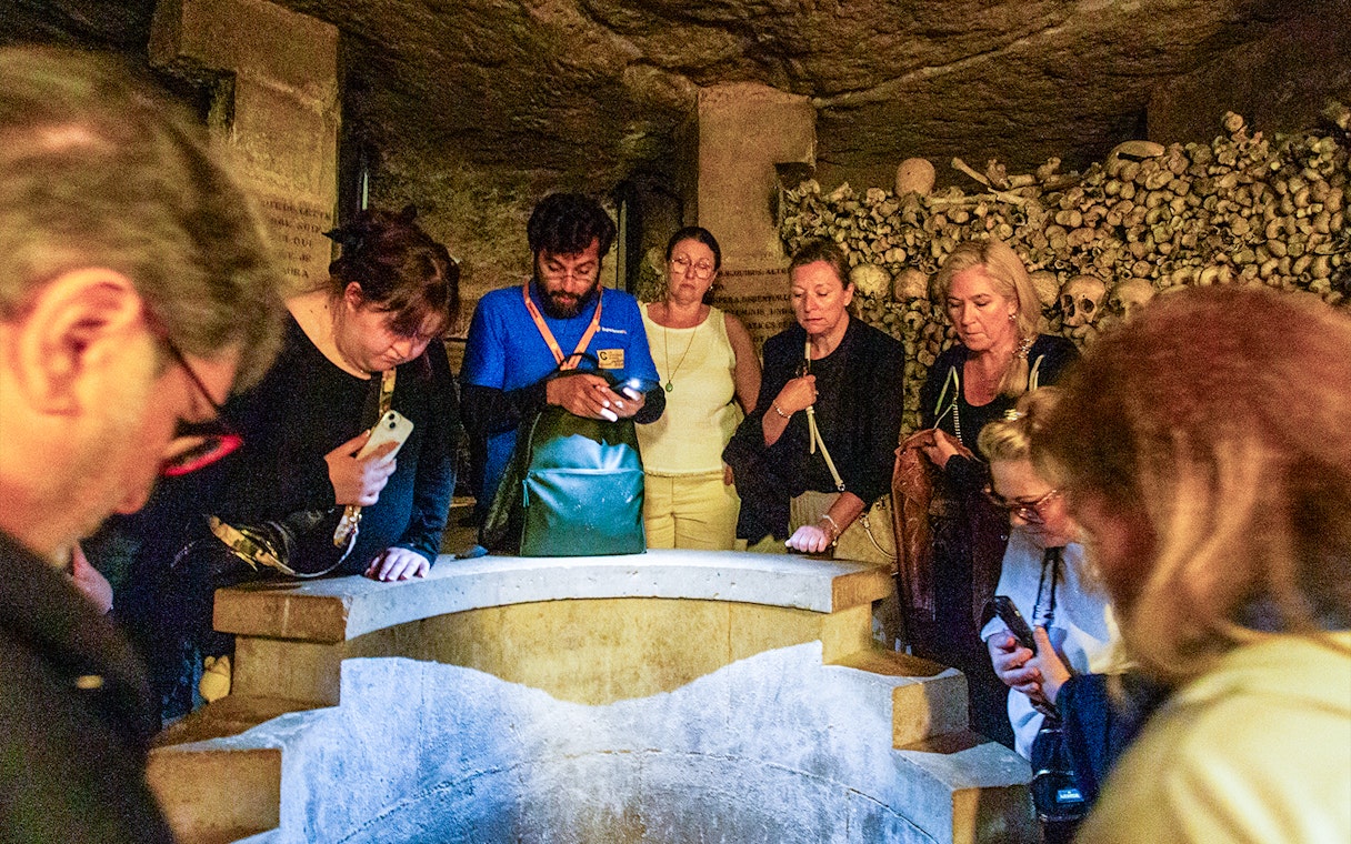 Tourists exploring the Paris Catacombs, viewing skulls and bones in dimly lit tunnels.