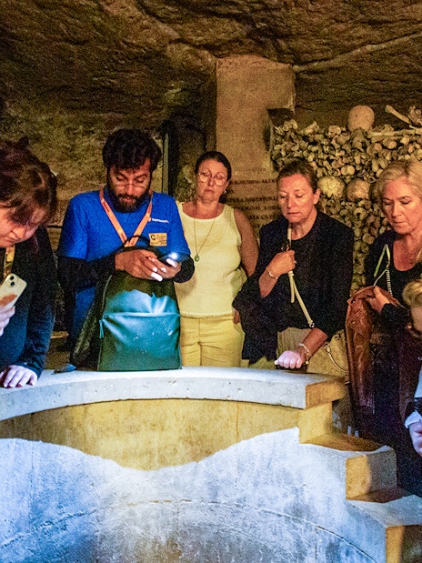 Tourists exploring the Paris Catacombs, viewing skulls and bones in dimly lit tunnels.