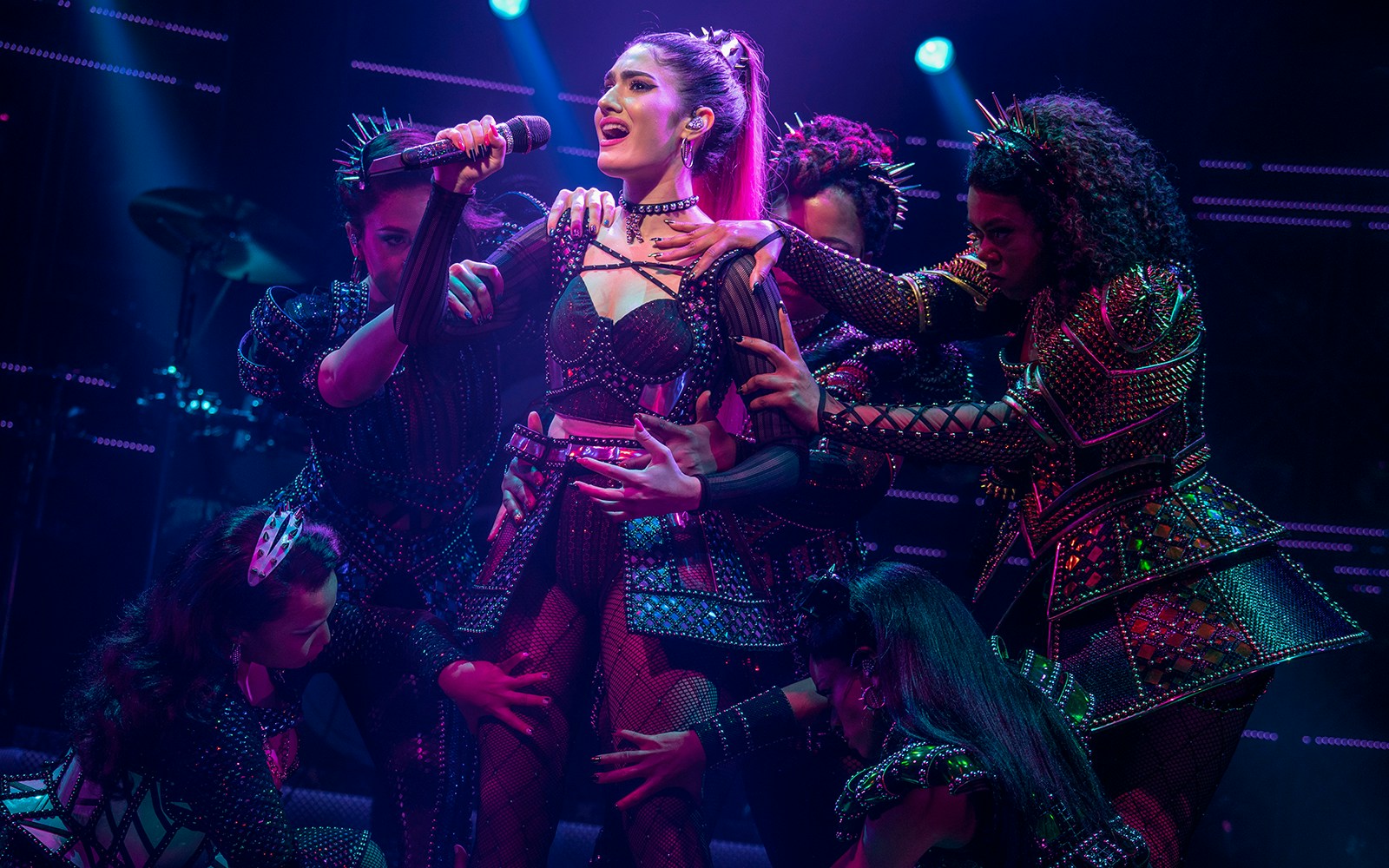 Performer singing on stage during SIX: The Musical with backup dancers.