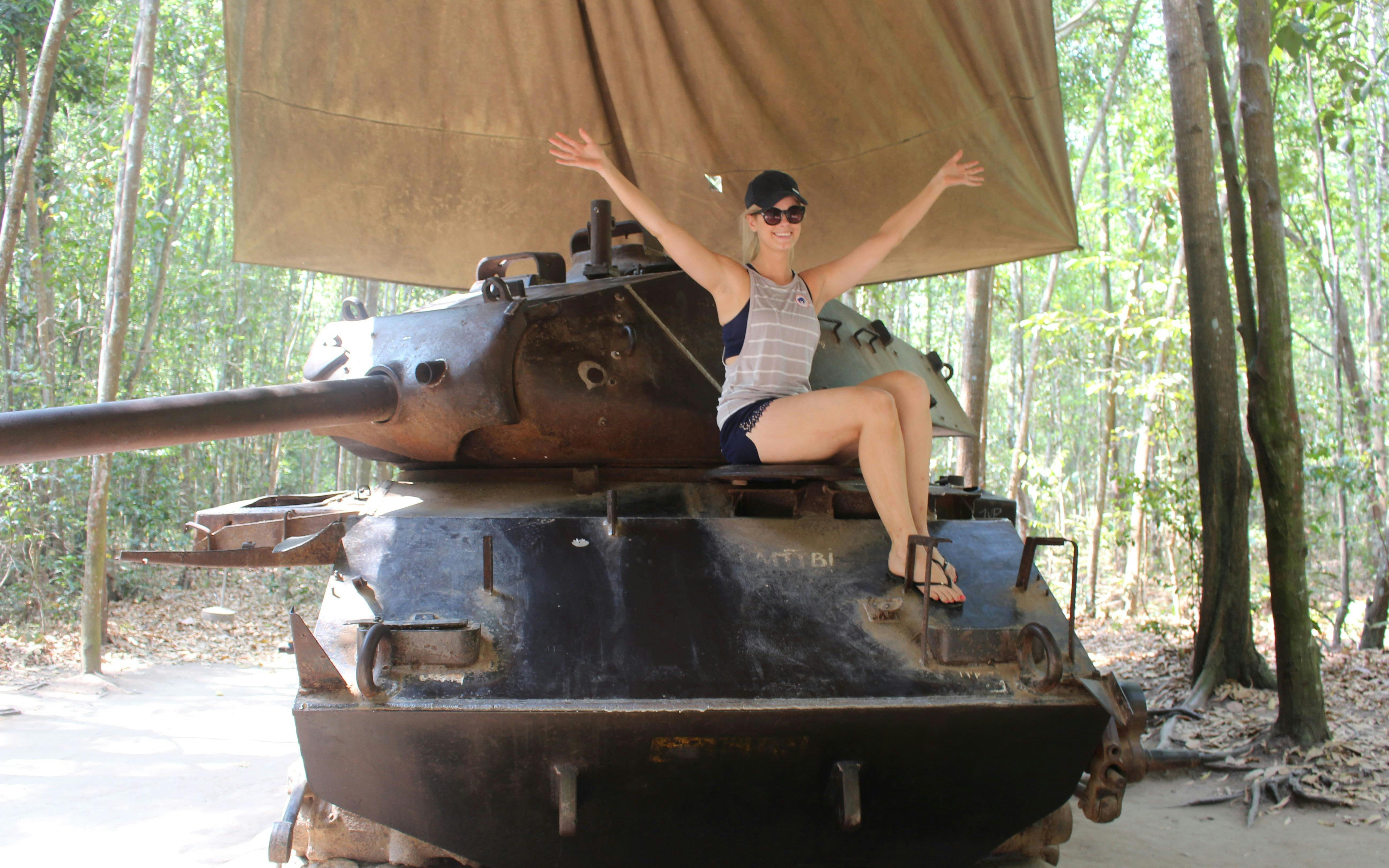 Person sitting on a tank at Cu Chi Tunnels, Vietnam, surrounded by forest.