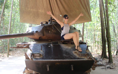 Person sitting on a tank at Cu Chi Tunnels, Vietnam, surrounded by forest.