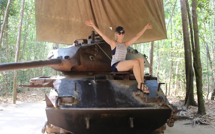 Person sitting on a tank at Cu Chi Tunnels, Vietnam, surrounded by forest.
